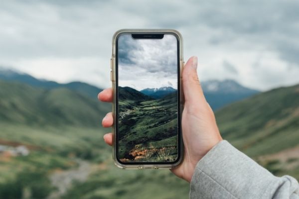 A smarphone held in a hand against nature, taking picture of the landscape