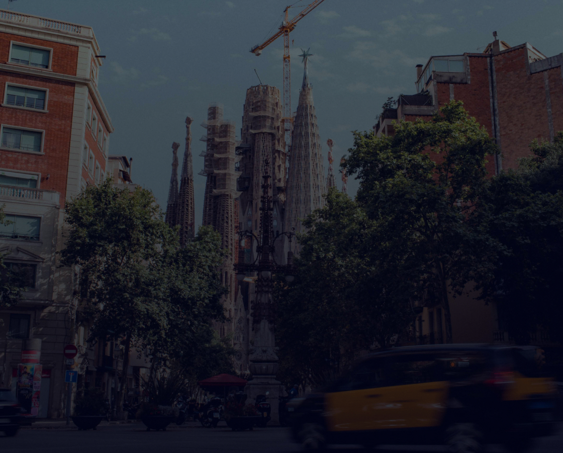 View of La Sagrada Familia from street, surrounded by trees and buildings
